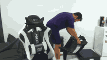 a man in purple shorts is standing next to a black and white maxf racer chair