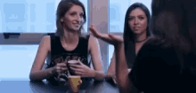 two women are sitting at a table with a cup of coffee and talking .