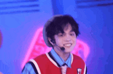 a young man wearing a red vest and tie is smiling and wearing a microphone .