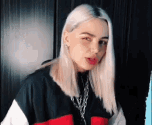 a woman with blonde hair is wearing a black , white and red jacket and a necklace .