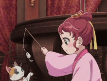 a girl in a pink kimono is playing with a cat on a fishing rod