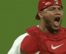 a baseball player wearing a red hat and catcher 's gear is yawning .