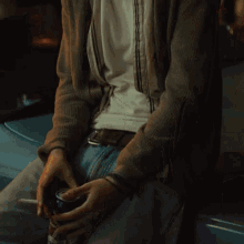 a man sitting on the hood of a car smoking a cigarette and holding a can of soda
