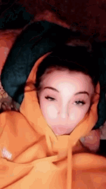 a woman wearing a yellow hoodie is laying on a bed with her head wrapped in a blanket .