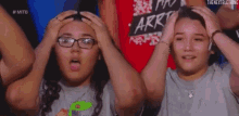 two young women are holding their heads in their hands while watching a wrestling match .