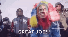 a man with rainbow hair is standing in front of a crowd of people and says `` great job '' .