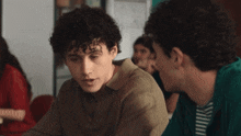 a man with curly hair talks to another man in a green shirt