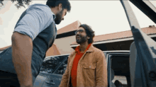two men are standing in front of a car and one has glasses on