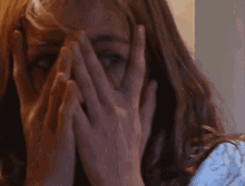 a woman covering her face with her hands while looking at the camera