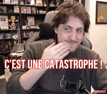 a man sitting in front of a microphone with the words " c'est une catastrophe " on the screen
