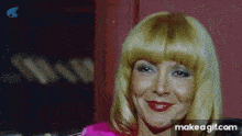 a woman with blonde hair and red lips is smiling in a pink dress .