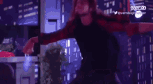 a woman in a red and black shirt is dancing in front of a city skyline .