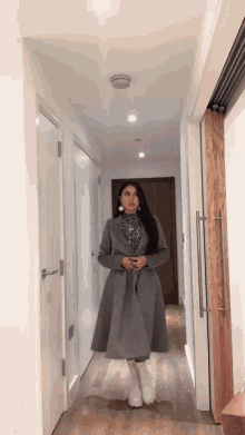 a woman wearing a grey coat and white boots is walking down a hallway