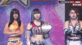 three women are standing on a stage with their arms crossed .