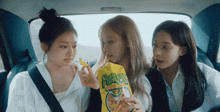 three girls are in a car eating a bag of fun n ' crunch chips