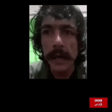 a man with long hair and a mustache is on a screen with a bbc logo