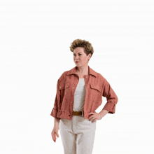 a woman in a pink jacket and white pants holds her hand up