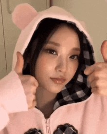 the girl is wearing a pink hoodie with ears and giving a thumbs up .