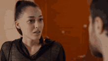 a woman in a ponytail talks to a man in a black shirt