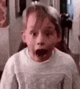 a young boy with his mouth open is making a surprised face .