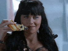 a woman with long black hair is eating a slice of pizza