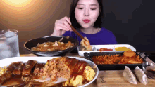 a woman in a blue shirt is eating a plate of food from a wooden table