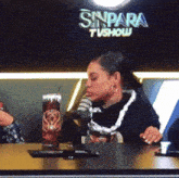 a woman is sitting at a table with a microphone in front of a sign that says sinpara tvshow