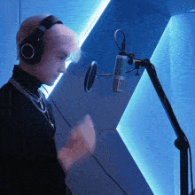a man wearing headphones and a necklace stands in front of a microphone on a stand which says vox