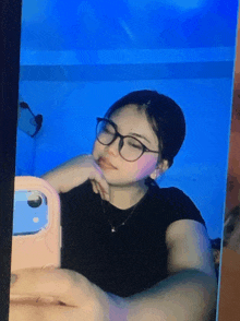 a girl wearing glasses is taking a selfie in a mirror