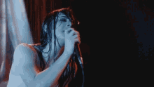 a woman singing into a microphone with a blue light behind her