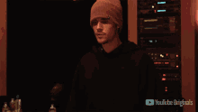 a man wearing a beanie and a black hoodie stands in front of a youtube originals logo