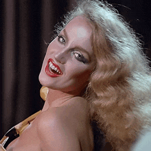 a woman with blonde hair and red lips is smiling with her mouth open