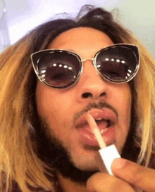 a man with a beard wearing sunglasses is applying lip gloss