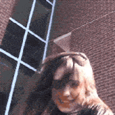 a woman is standing in front of a brick building and smiling .