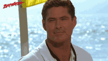 a man in a white shirt is standing in front of a yellow flag that says baywatch