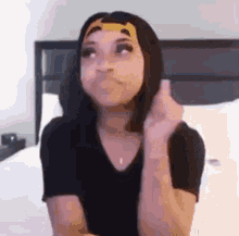 a woman in a black shirt is sitting on a bed and holding her hair .