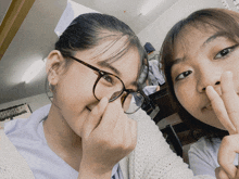 two girls wearing glasses covering their faces with their fingers