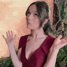 a woman in a red dress is standing in front of a tree with her hands outstretched .