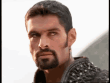 a man with a beard and earrings is wearing a black jacket with studs on it .