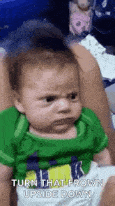 a baby in a green shirt is making a funny face while being held by a woman .