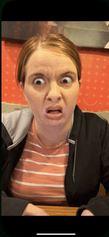 a woman wearing a striped shirt and a black jacket makes a funny face