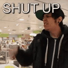 a man wearing a hat and a black jacket is standing in front of a sign that says shut up