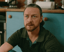 a man with a beard is sitting on the floor in front of a kitchen counter .