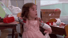 a little girl in a pink dress is sitting on a rocking chair in front of a book and a red speaker