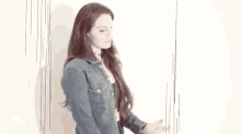 a woman in a denim shirt is leaning against a wall and looking at her watch .