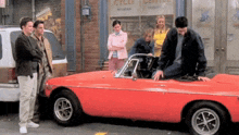 a group of people are standing around a red car in front of a store that says cycle center