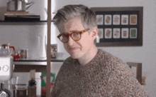a man wearing glasses and a sweater is making a funny face in a kitchen .