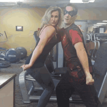 a man and a woman pose for a picture in a gym with a machine that says nautilus on it