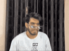 a man wearing a white shirt and glasses is standing in front of a black curtain .