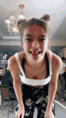 a woman in a white tank top and black pants is standing in a room with her tongue hanging out .
